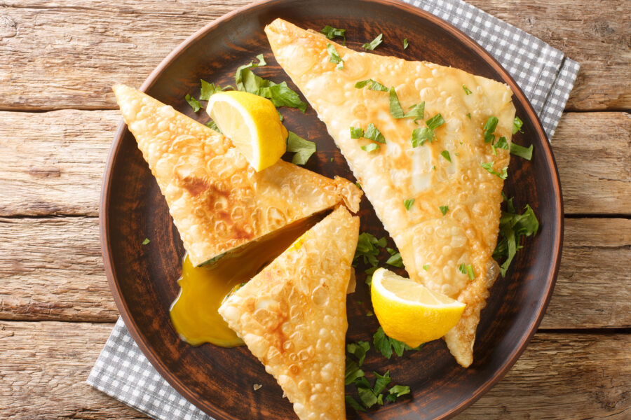 Brik is a very thin, brittle pastry used in Tunisian cooking is the base for a breakfast pastry stuffed with egg, potato, tuna fish close up in the plate on the wooden table. Horizontal top view