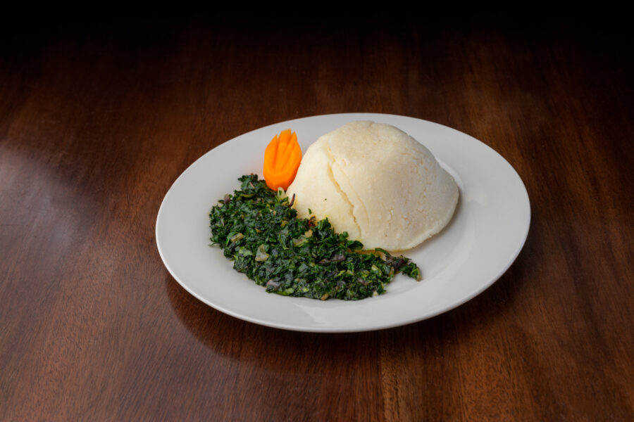 Ugali / Cornmeal Mush and vegetable dish served on a white plate on a wooden table.