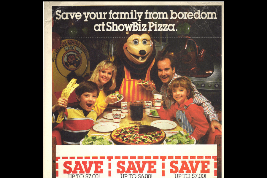 This nostalgic advertisement for ShowBiz Pizza depicts a smiling family enjoying a meal with pizza, salad, and drinks, joined by Billy Bob, the animatronic bear mascot, in a lively arcade atmosphere.