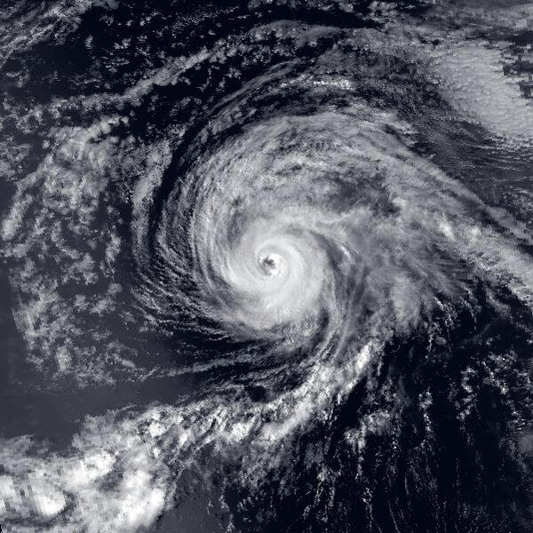 Black and white satellite image of a swirling hurricane over the ocean, with a clearly defined eye at the center and dense spiral cloud bands radiating outward in a powerful, organized formation.